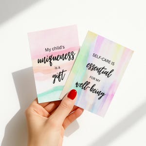May include: Two cards with watercolor backgrounds are held in a hand. One card reads "My child's uniqueness is a gift." The other card says "Self-care is essential for my well-being."