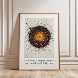 May include: A framed wall art print featuring a central circular burst of multicolored dots in shades of yellow, orange, red, and black on a cream background. Below the graphic, the text reads: My Brain's Dopamine Fires to Its Own Beautiful Rhythm.