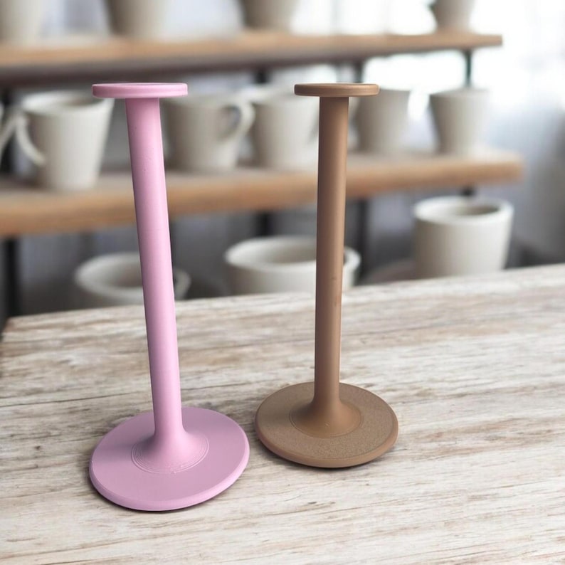 May include: Two decorative stands, one pink and one brown, with a round base and a tall, cylindrical stem. The stands are made of a smooth, solid material.