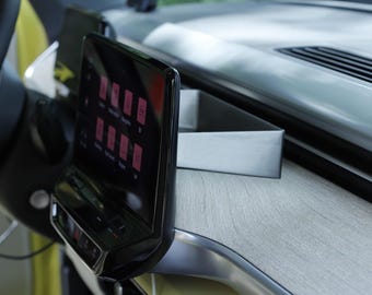 Op de afbeelding: Detail van een auto-interieur met een zwart touchscreen met roze pictogrammen. Het dashboard heeft een licht houteffect en zilveren afwerking. Een stuurwiel is zichtbaar aan de linkerkant.