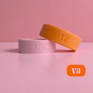 Può includere: Due anelli in silicone, uno arancione e uno bianco. L'anello arancione ha il numero "12" stampato su di esso. L'anello bianco ha il testo "3DLABCS" stampato su di esso.