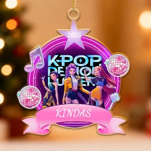 May include: A K-Pop themed Christmas ornament with a star shape at the top and a pink banner at the bottom that says "KINDAS". The ornament features three animated figures, disco balls, and the text "KPOP REUNION" in a purple circle.