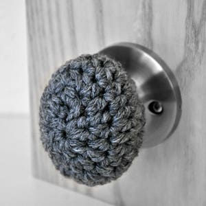 May include: A grey crocheted door knob cover with a silver door knob.