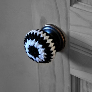 Peut inclure: Un cache-poignée de porte en crochet noir et blanc. Le cache est fixé à une poignée de porte noire.