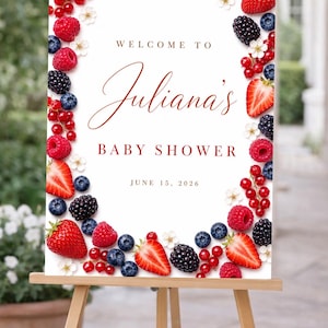Pode incluir: Uma placa retangular branca com uma borda de morangos, mirtilos, framboesas, amoras, groselhas vermelhas e pequenas flores brancas. O texto diz: WELCOME TO Juliana's BABY SHOWER JUNE 15, 2026, em letras vermelho-escuras e castanhas.