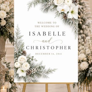 May include: A rectangular wedding welcome sign on a gold easel featuring white roses, orchids, and frosted pine branches with pinecones. The text reads: WELCOME TO THE WEDDING OF ISABELLE and CHRISTOPHER DECEMBER 14, 2041, in black and gold lettering.