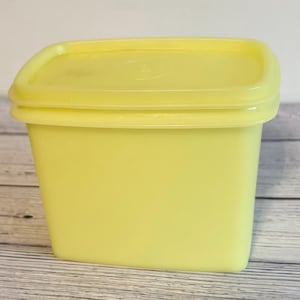 May include: A vintage, pale yellow rectangular container with a matching lid. The container has a slightly curved top and a smooth, matte finish. The lid fits snugly, creating a tight seal. This storage container is ideal for kitchen or pantry organization.