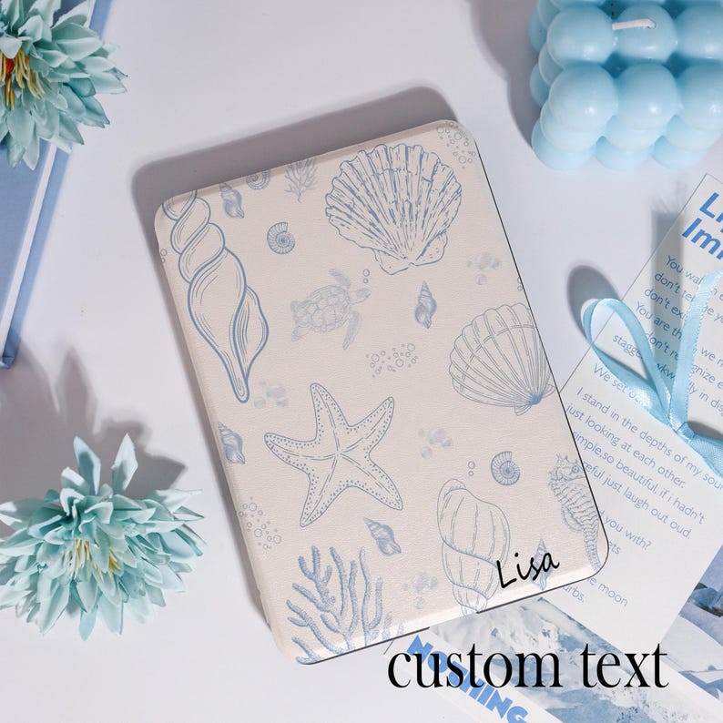 Puede incluir: Una funda rectangular blanquecina con un dise&ntilde;o azul de conchas marinas y estrellas de mar. La funda tiene los textos "Lisa" y "custom text" impresos. El dise&ntilde;o incluye varias criaturas marinas y coral.