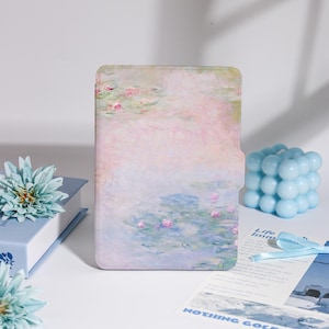 Può includere: Una custodia rettangolare con un dipinto ad acquerello pastello di ninfee. La custodia è rosa chiaro, blu e verde. Una candela a cubo a bolle azzurra e un fiore blu sono anche nell'immagine.