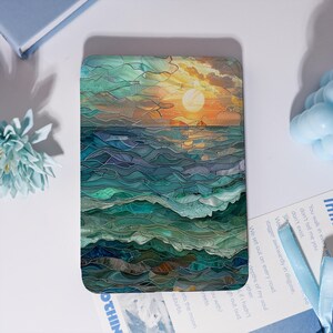 May include: A rectangular e-reader cover featuring a stained glass style illustration of an ocean sunset. The design displays layered teal, blue, and green waves beneath a golden sun and clouds, rendered in a segmented, mosaic-like pattern.
