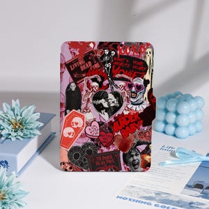 May include: A rectangular case adorned with horror-themed stickers. The stickers depict skeletons, hearts, coffins, and phrases such as "Living Dead Girl" and "Murder Baby." The background is a blend of pink and red.