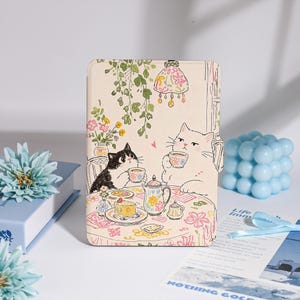 May include: A beige tablet case with a charming illustration of two cats at a tea party. The design includes floral patterns, a teapot, and cake. The case has a soft pastel colour scheme with pink, green, and yellow details.