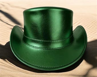 Puede incluir: Un sombrero de copa verde esmeralda brillante, con ala ancha y una banda alrededor de la corona. El sombrero está hecho de un material liso. El sombrero está sobre una superficie arenosa.