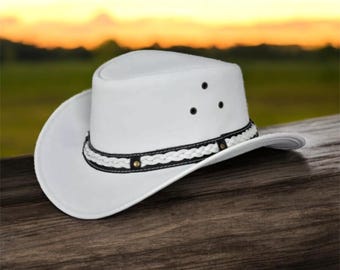 May include: A white cowboy hat with a braided black and white band and decorative rivets. The hat has a wide brim and three small air vents on the crown. The hat is made of a sturdy material and is suitable for outdoor wear.