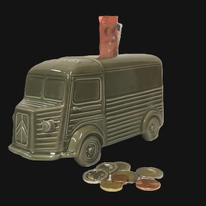 May include: A sage green ceramic money box shaped like a vintage delivery van with a slot on the roof containing a fifty euro banknote. Several assorted metal euro coins are scattered in front of the vehicle, which features a ribbed body.