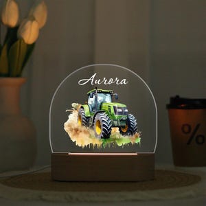 May include: A night light with a green tractor design and yellow wheels. The tractor is set against a watercolour-style background. The name "Aurora" is written in cursive at the top of the light.
