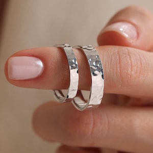 Può includere: Due orecchini a cerchio in argento martellato, uno leggermente più grande dell'altro, indossati su un dito.