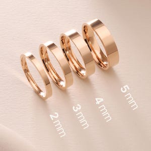 Puede incluir: Cuatro anillos de tono oro rosa dispuestos en fila, cada uno con un ancho de banda diferente. Los anillos tienen texto que indica sus anchos como 2 mm, 3 mm, 4 mm y 5 mm. Los anillos tienen un acabado de superficie liso, pulido y reflectante.