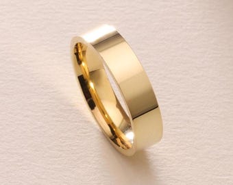 May include: A gold-colored ring with a flat, rectangular band. The ring has a polished, reflective surface, and the interior is also gold. The ring is a simple, elegant design.