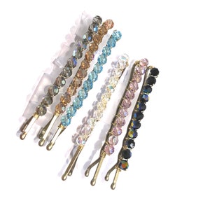 May include: Six beaded hair clips in various colors, including black, pink, white, blue, brown, and gray. The clips are made of metal and have a double prong design.
