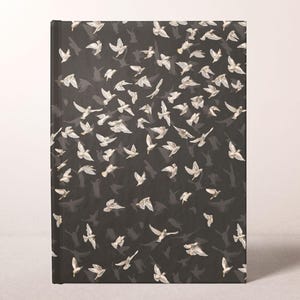 May include: A hardcover journal with a black cover featuring a pattern of white birds in flight. The birds are depicted with detailed wings and are scattered across the cover, creating a sense of movement and freedom.