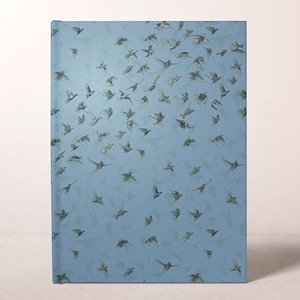 May include: A hardcover journal with a light blue cover featuring a pattern of flying birds. The birds are depicted in shades of gray and brown, creating a sense of movement against the blue background. The journal is rectangular and appears to be new.