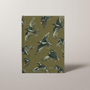 May include: A hardcover journal with a repeating pattern of birds in flight. The birds are depicted in shades of gray, white, and red against an olive green background. The journal is rectangular and stands upright.