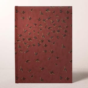 May include: A hardcover journal with a burgundy cover featuring a pattern of numerous birds in flight. The birds are depicted in shades of brown and black, creating a dynamic and artistic design. The journal is a rectangular shape.