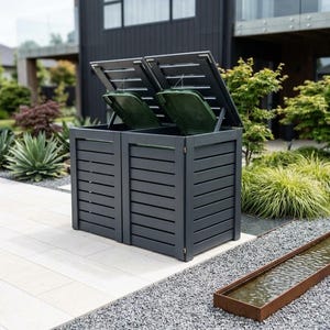 May include: A double-compartment outdoor storage unit featuring dark grey horizontal slats and two hinged lids that open to reveal green bin covers. The structure is rectangular with a clean, slatted design, providing a secure enclosure for waste bins.