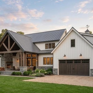 May include: A two-story house with white vertical siding, a dark metal roof, and a stone foundation. The exterior features a covered porch with a stone fireplace, a dark brown garage door with windows, and a gravel driveway set on a green lawn.