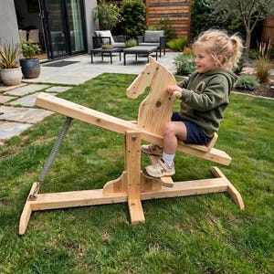 May include: A wooden rocking horse toy featuring a natural light wood finish, a horse-shaped head, a horizontal seat, and a metal spring mechanism attached to the base frame, designed for outdoor use on a grassy lawn surface.