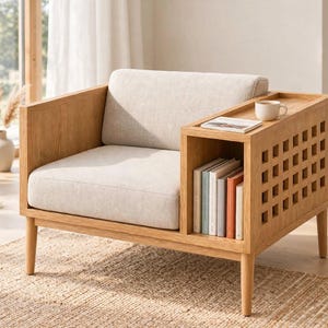 May include: A light oak wood armchair featuring a beige upholstered seat and back cushion. The right armrest is extended into a functional side table with a built-in storage compartment underneath, containing several books and a small white mug.