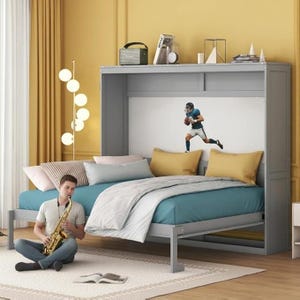 May include: A grey wall-mounted Murphy bed featuring a white back panel with a graphic of a football player in motion. The bed is dressed with a teal sheet, a white blanket, and two mustard yellow pillows. A person sits on the floor playing a saxophone.