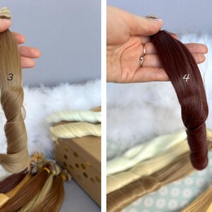 May include: Two bundles of hair extensions, one light brown with the number 3, and the other dark red with the number 4. The extensions are held up against a white fluffy background, with other bundles of hair in various shades.
