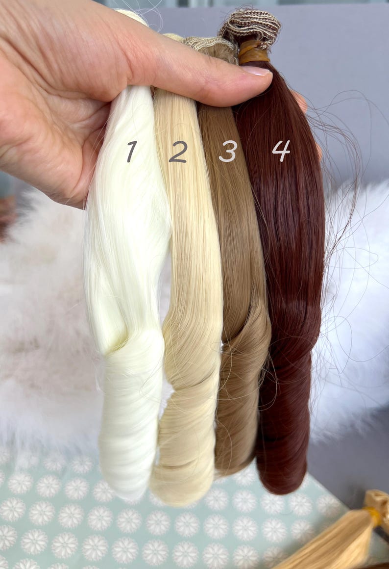 May include: Four bundles of hair extensions in varying shades of blonde and brown. The colors are numbered 1 through 4, with the first being a light blonde, followed by a medium blonde, a light brown, and a dark auburn. The extensions are held together at the top.