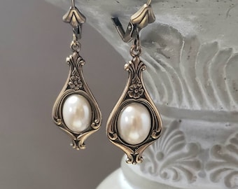 May include: A pair of gold tone earrings with a pearl drop. The earrings have a floral design and are a classic style.