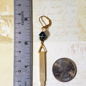 K&ouml;nnte beinhalten: Goldene Ohrh&auml;nger mit einem blauen und gr&uuml;nen facettierten Glasperlen und einem goldenen geometrischen Design. Die Ohrringe sind etwa 5 cm lang.