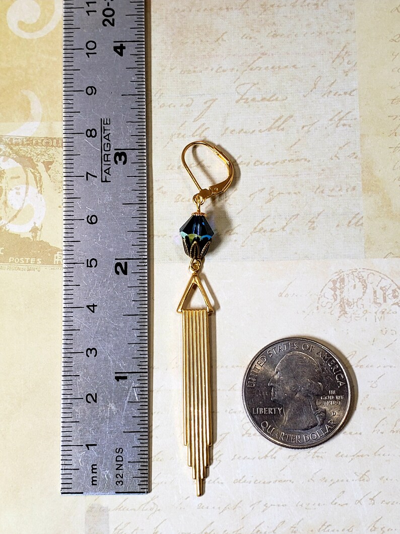 K&ouml;nnte beinhalten: Goldene Ohrh&auml;nger mit einem blauen und gr&uuml;nen facettierten Glasperlen und einem goldenen geometrischen Design. Die Ohrringe sind etwa 5 cm lang.