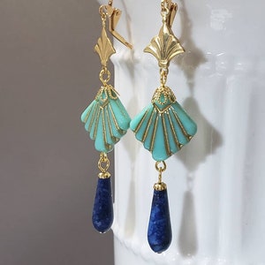 May include: A pair of gold-tone drop earrings featuring a fan-shaped turquoise bead with gold detailing, topped with a gold metal fan accent, and finished with a dangling dark blue teardrop-shaped stone bead suspended from a gold-tone leverback.