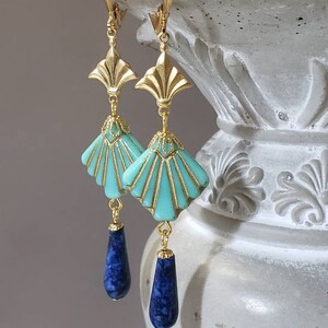 May include: A pair of gold-tone drop earrings featuring a fan-shaped turquoise-coloured component with gold-tone detailing, suspended from a gold-tone metal top piece, and finished with a dangling dark blue teardrop-shaped stone at the bottom.