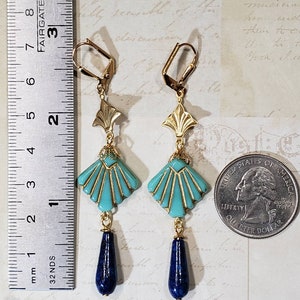 May include: A pair of gold-tone dangle earrings featuring a turquoise fan-shaped bead with gold accents and a dark blue teardrop-shaped stone at the base. A metal ruler shows the earrings are approximately 8.3 cm long next to a US quarter coin.