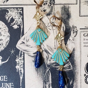 May include: A pair of gold-tone leverback earrings featuring a fan-shaped turquoise enamel component with gold detailing, suspended from a gold fan-shaped connector and finished with a dangling dark blue teardrop-shaped bead with a marbled texture.