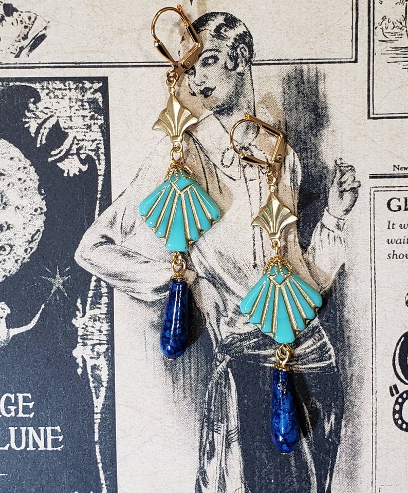 May include: A pair of gold-tone leverback earrings featuring a fan-shaped turquoise enamel component with gold detailing, suspended from a gold fan-shaped connector and finished with a dangling dark blue teardrop-shaped bead with a marbled texture.
