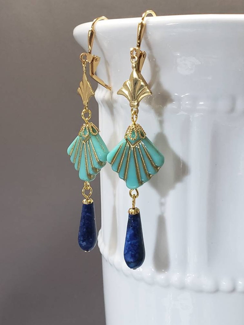 May include: A pair of gold-tone leverback earrings featuring a fan-shaped turquoise bead with gold-tone detailing, suspended from a gold-tone metal accent, and finished with a dark blue teardrop-shaped stone bead at the bottom of each earring.