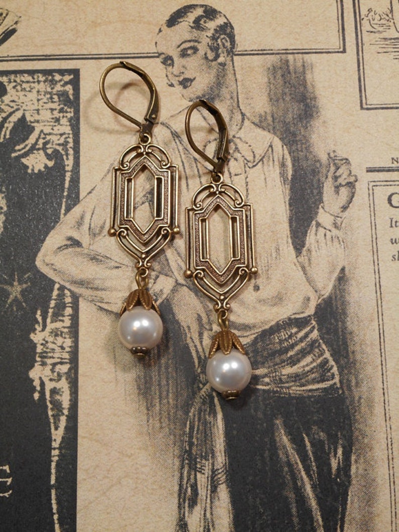 May include: A pair of gold-tone earrings with a geometric design and a single pearl drop on each earring.