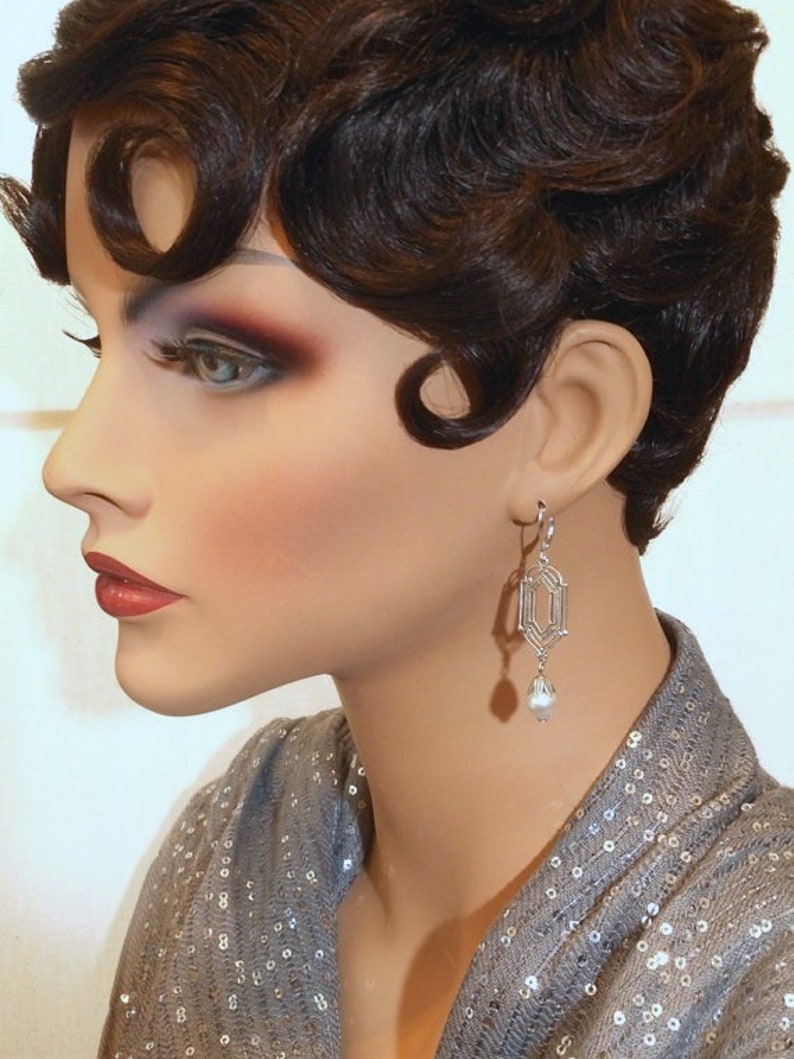 May include: A silver geometric dangle earring with a pearl drop. The earring is worn by a mannequin with short, dark brown hair styled in a 1920s bob.