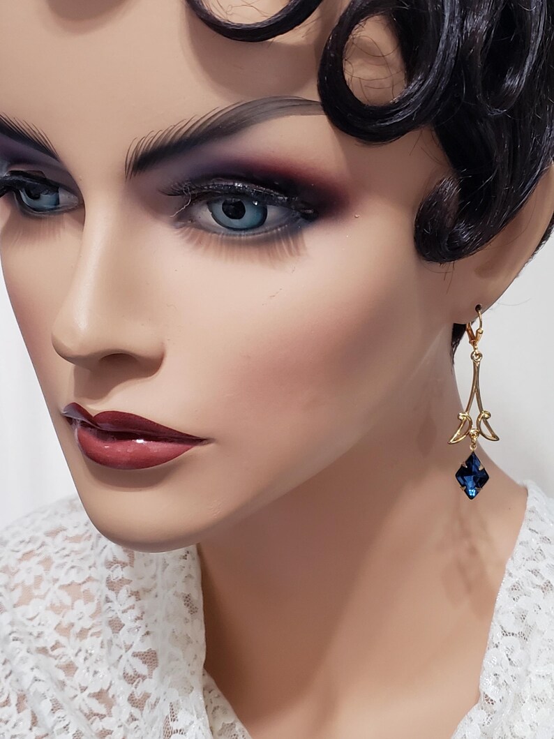 May include: Gold dangle earrings with a blue crystal teardrop. The earrings feature a delicate, intricate design.