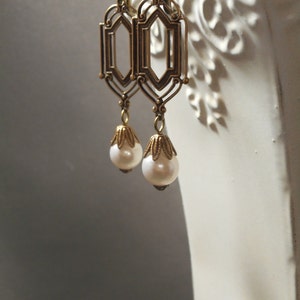 May include: A pair of gold-tone dangle earrings with a geometric design and a white pearl drop.