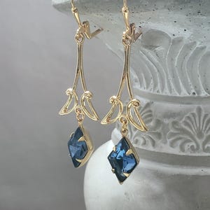 May include: Gold dangle earrings with a blue gemstone pendant. The earrings have a delicate, ornate design.