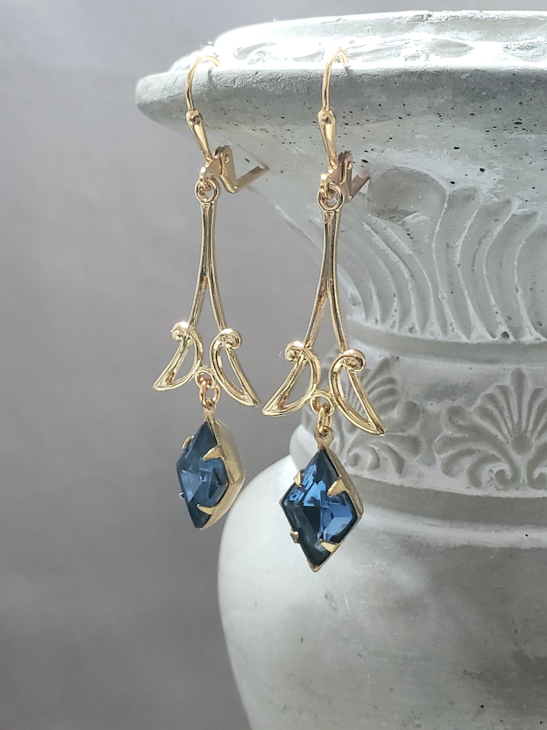 May include: Gold dangle earrings with a blue gemstone pendant. The earrings have a delicate, ornate design.